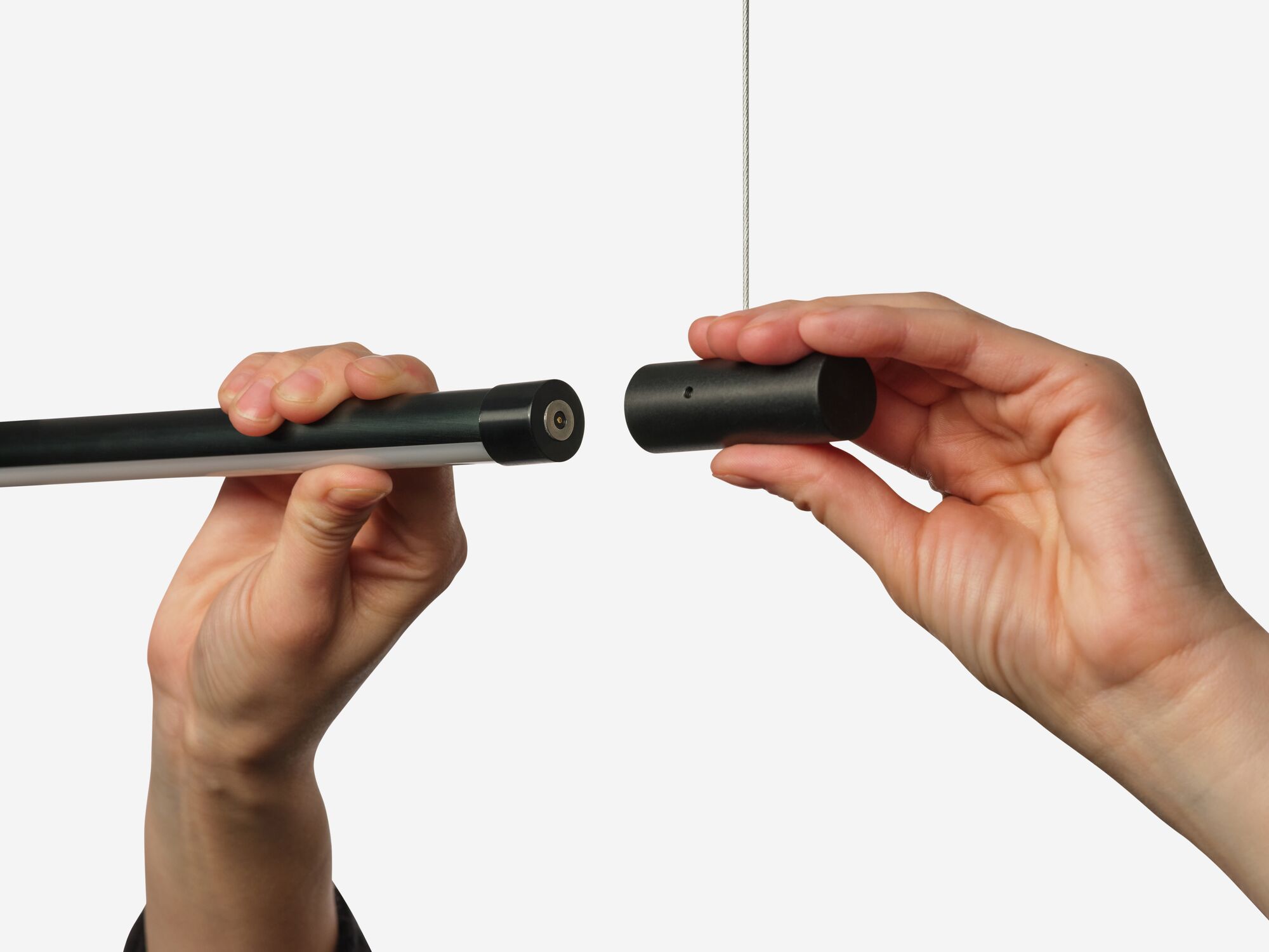 Hands connecting slim black pendant light to connector